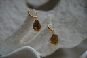 Gold-tone hoop earrings with teardrop charms, round clear accents and sunburst markings.