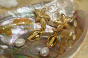 Gold-tone drop earrings with dotted starfish tops, cowrie motifs and white bead drops.