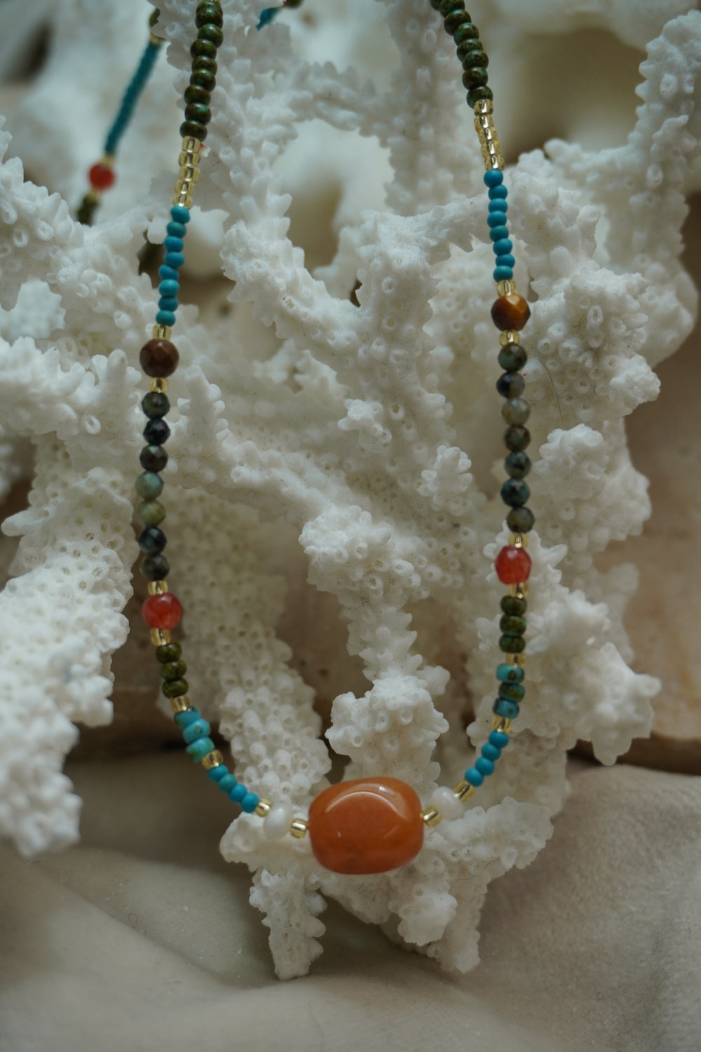Alternate view: multicoloured bead necklace with a large rounded orange centre bead and small white beads at either side.