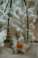 Alternate view: multicoloured bead necklace with a large rounded orange centre bead and small white beads at either side.