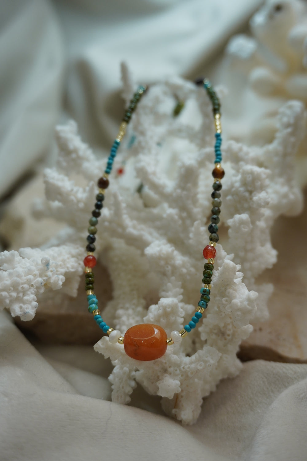 Multicoloured bead necklace with a large rounded orange centre bead and small white beads at either side.