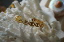 Gold-tone open cuff formed from repeated eye shapes with round centres and dotted borders.