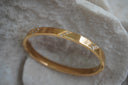Gold-tone bangle with diagonal rows of clear accents across a smooth band.