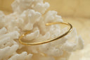 Alternate view: gold-tone open cuff with a smooth rounded profile and tapered ends.