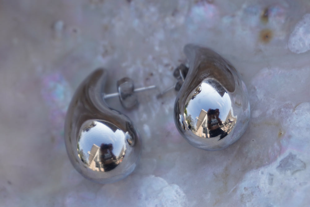 Silver-tone teardrop stud earrings with rounded bases, curved tips and visible posts.