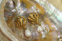 Gold-tone sculpted stud earrings with curving raised ridges and white drop-shaped beads.
