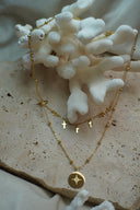 Layered gold-tone necklace arrangement with small cross drops above a bead-station chain and a star-marked round disc.