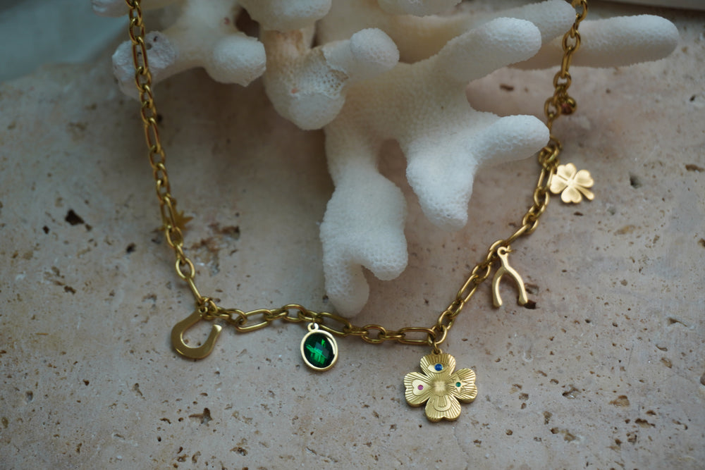 Gold-tone link necklace with horseshoe, wishbone and clover charms, a green oval accent and multicoloured details.