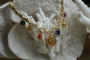 Necklace with pale pink braided cord, gold-tone chain, multicoloured bead drops, sun charms and an eye-patterned disc.