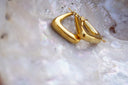 Alternate view: gold-tone rounded triangular hoop earrings with smooth reflective surfaces.