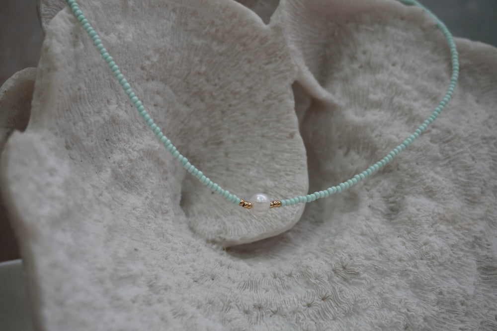 Alternate view: pale-aqua seed-bead necklace with a white centre bead and small gold-tone spacers.