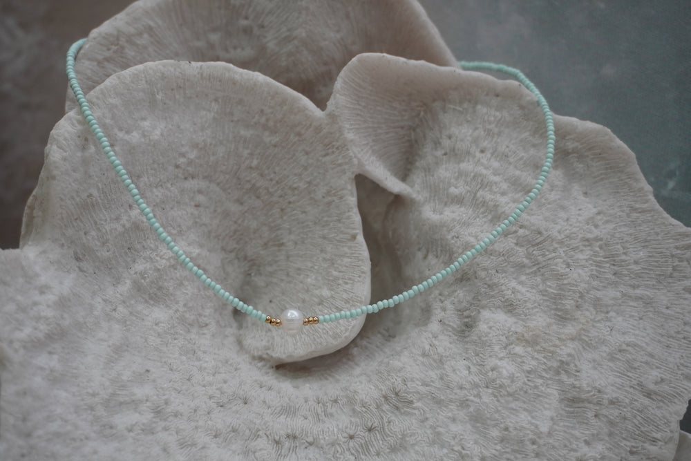 Pale-aqua seed-bead necklace with a white centre bead and small gold-tone spacers.