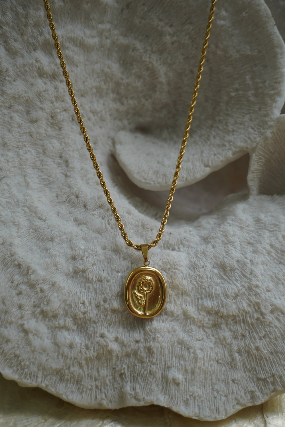 Alternate view: gold-tone oval flower pendant with a raised stem and leaf on a twisted necklace chain.