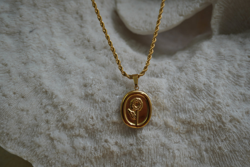 Gold-tone oval flower pendant with a raised stem and leaf on a twisted necklace chain.