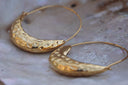 Alternate view: gold-tone hoop earrings with fine circular wires and broad dimpled crescent-shaped lower sections.