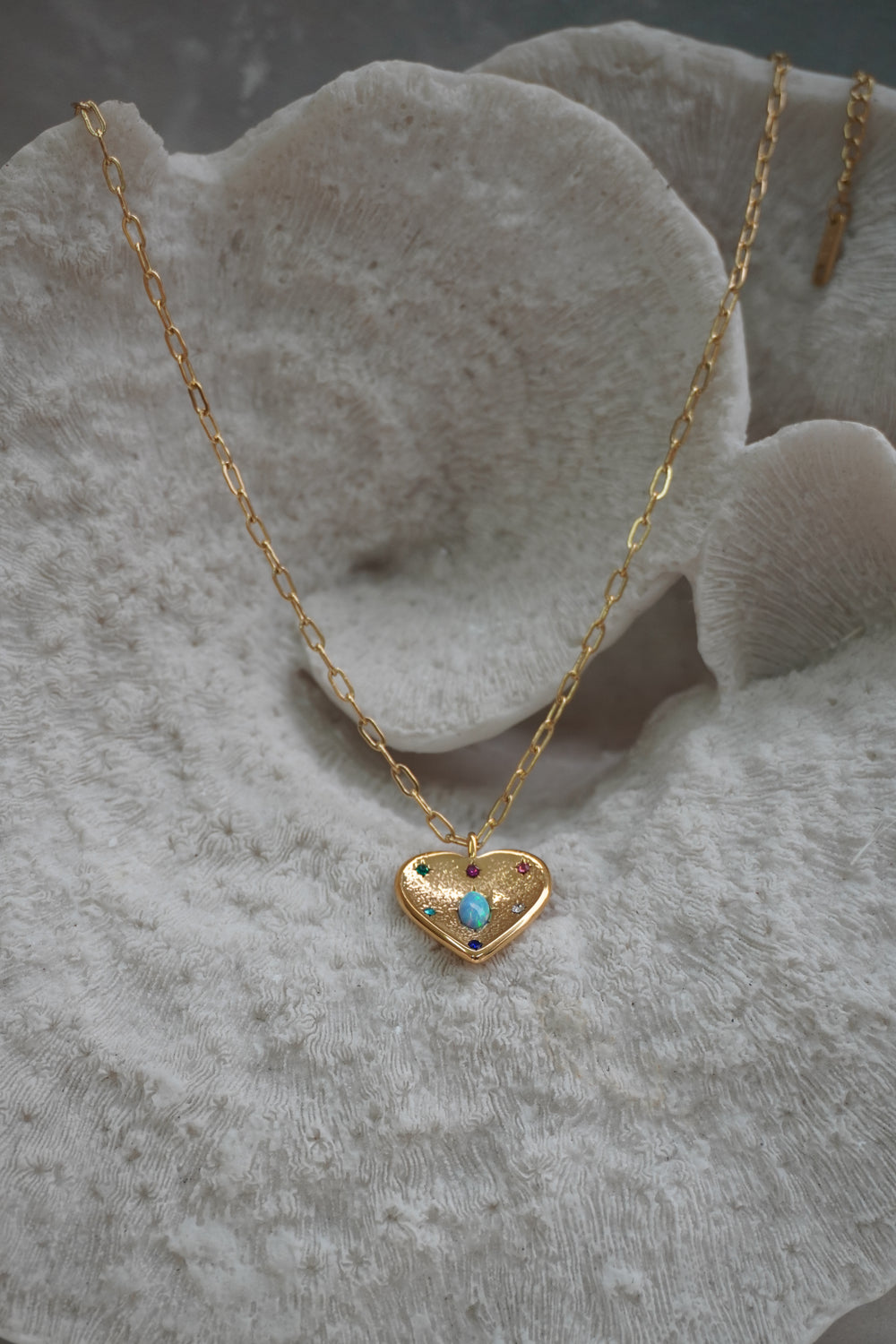 Gold-tone heart necklace with a blue-green iridescent oval, coloured accents and elongated chain links.