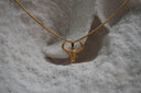 Gold-tone necklace with a narrow horned skull pendant, raised forehead details and a closely linked chain.