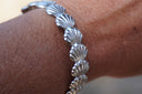 On-wrist detail of repeating ridged fan-shell motifs on a silver-tone cuff.