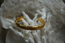 Alternate view: gold-tone open cuff with smooth sections and raised diagonal bands.