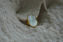 Ring with a gold-tone border and band around an irregular pale iridescent centre.