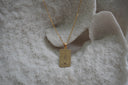 Gold-tone necklace with a rectangular Wheel of Fortune pendant showing crossed fingers and X lettering.