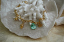 Gold-tone link bracelet with starfish, strawberry and fish charms beside an irregular green bead.