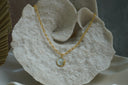 Gold-tone oval-link necklace with a sun face and curved rays on a pale disc.