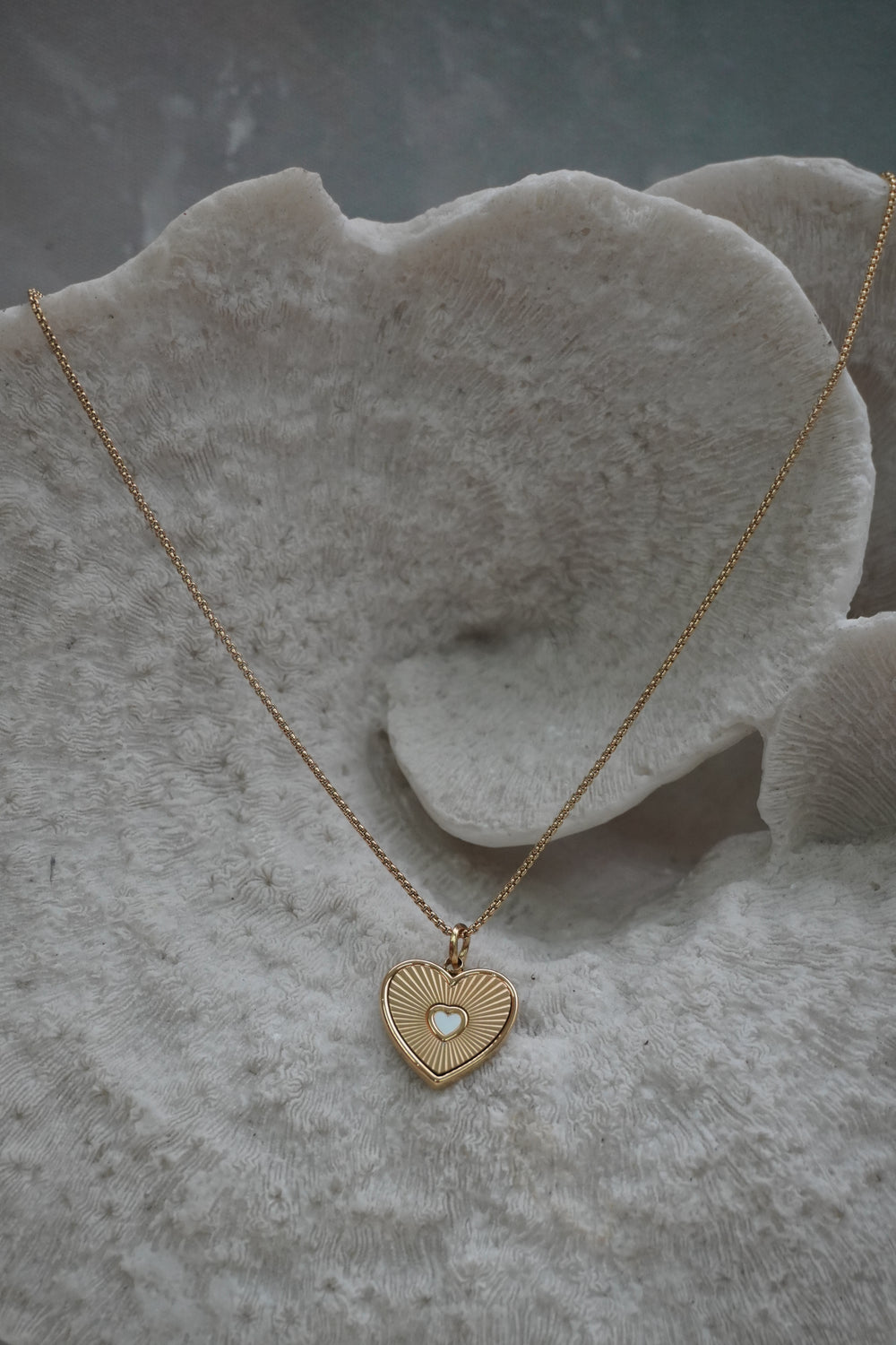 Gold-tone necklace with a heart pendant, radiating lines and a small pale heart at the centre.