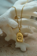 Gold-tone chain necklace with an irregular arched tag, raised four-point star motif and radiating lines.