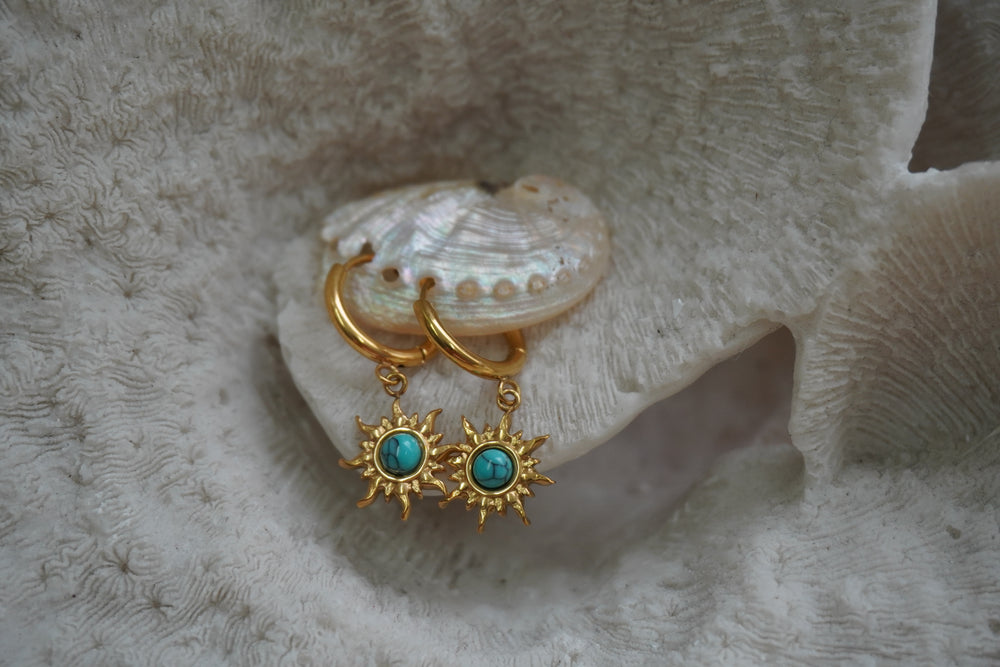 Gold-tone hoop earrings with sunburst charms and blue centres marked by dark vein-like lines.