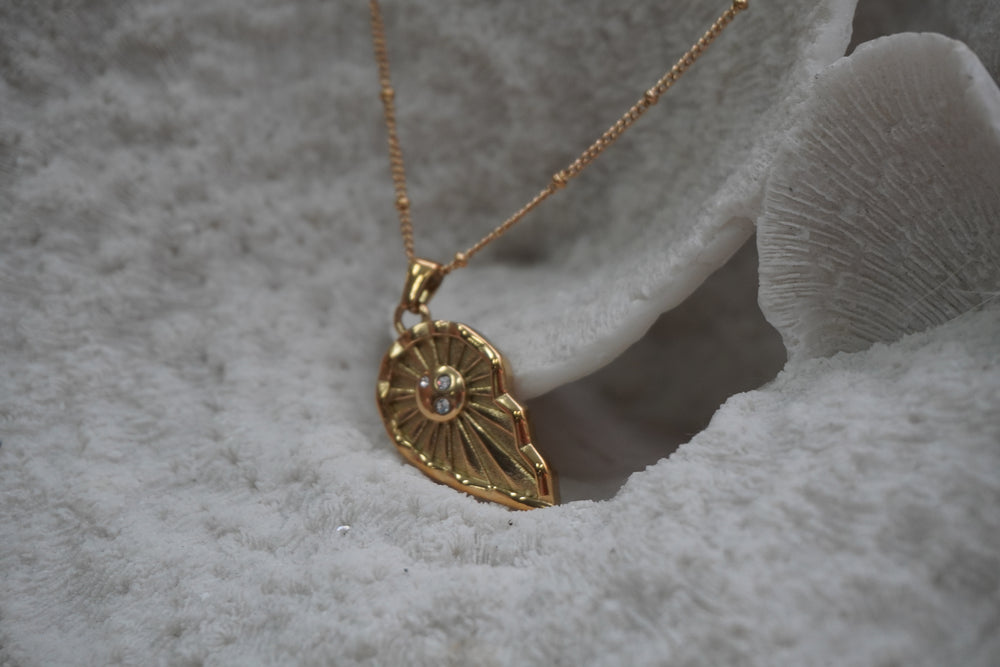 Alternate view: gold-tone necklace with an asymmetric pointed pendant, radiating lines and clear accents at its oval centre.