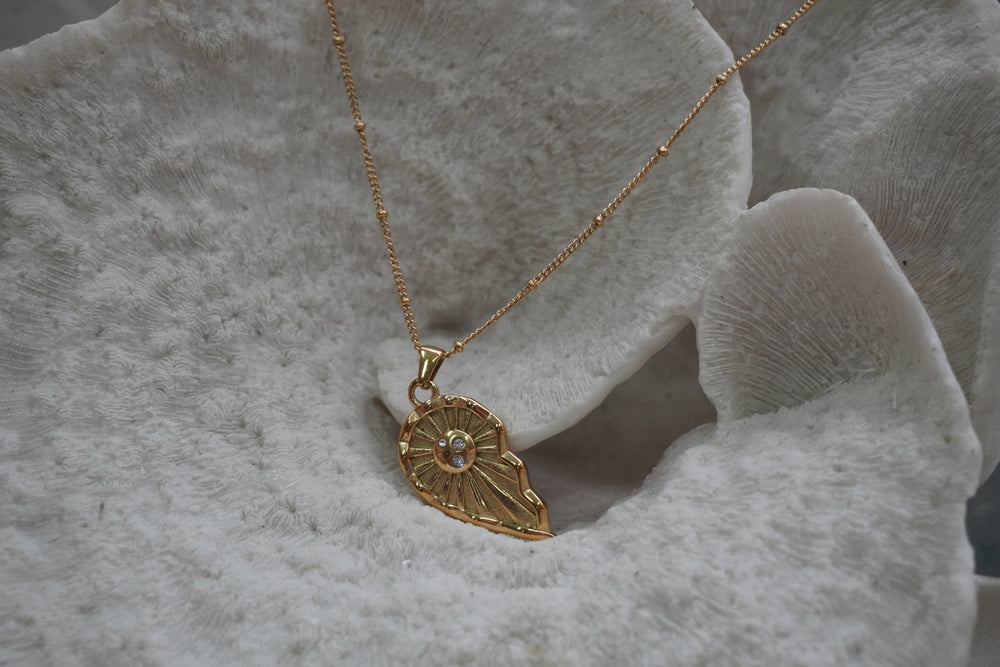 Gold-tone necklace with an asymmetric pointed pendant, radiating lines and clear accents at its oval centre.