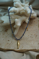 Blue round-bead necklace with a textured gold-tone fish pendant and small gold-tone disc charms.