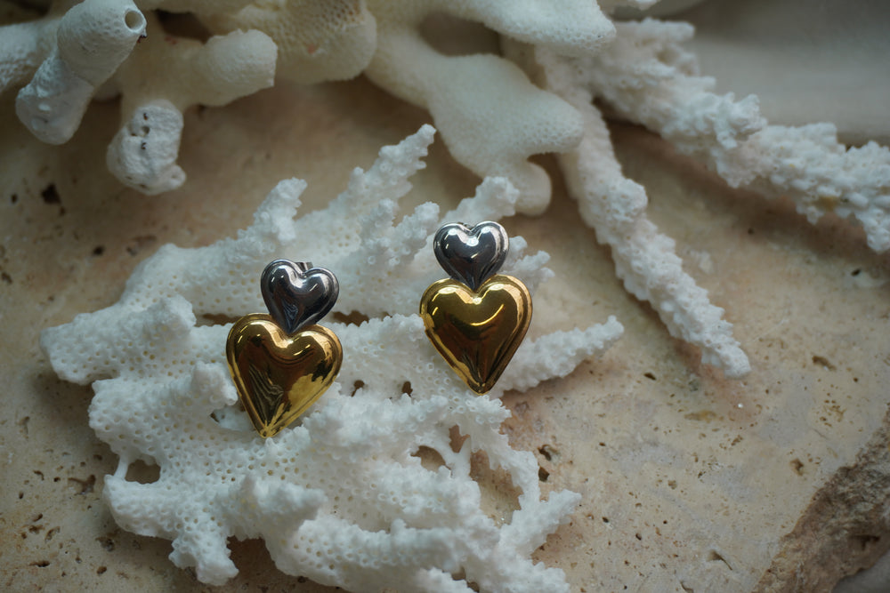 Earrings with a small silver-tone heart above a larger reflective gold-tone heart.