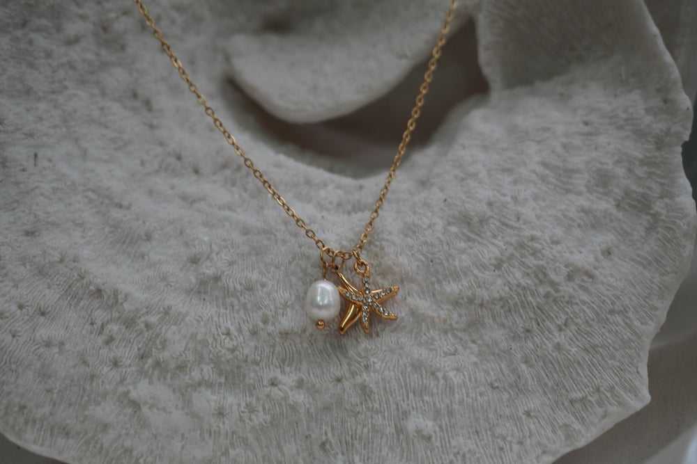 Gold-tone necklace with two overlapping starfish charms, clear accents and a white oval bead.