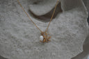 Gold-tone necklace with two overlapping starfish charms, clear accents and a white oval bead.