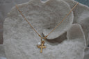 Gold-tone necklace with a patterned cross charm and white oval beads suspended from a front ring.